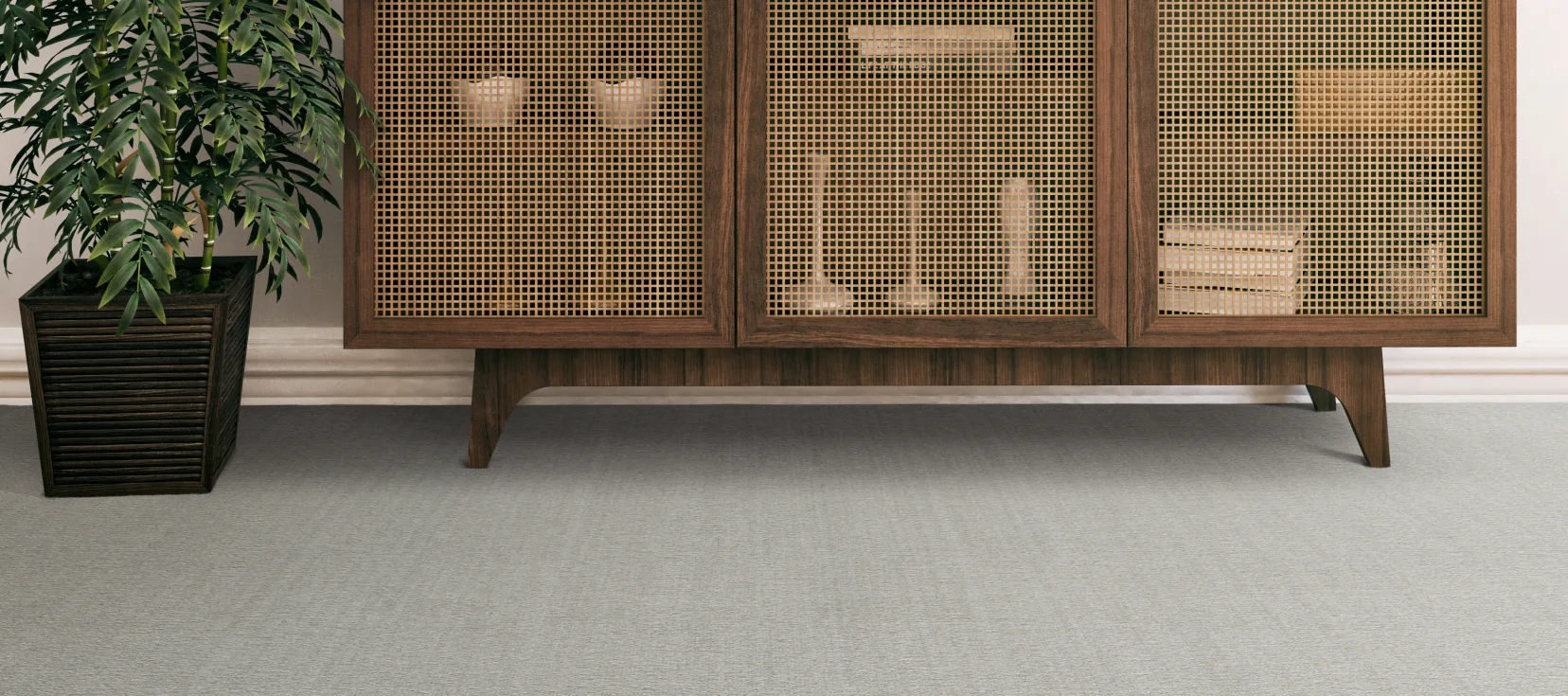 A stylish interior scene with Engineered Floors Carpet in a light gray color. A wooden cabinet with a woven rattan front stands beside a lush potted plant.
